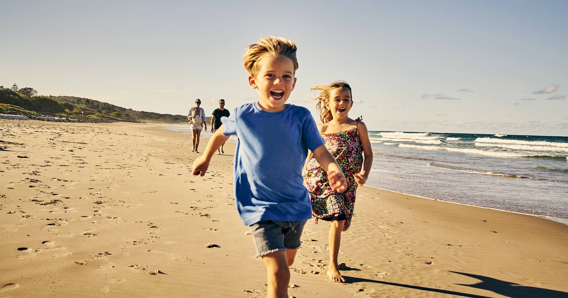 Uśmiechnięte dzieci biegną po plaży przed swoimi spacerującymi rodzicami