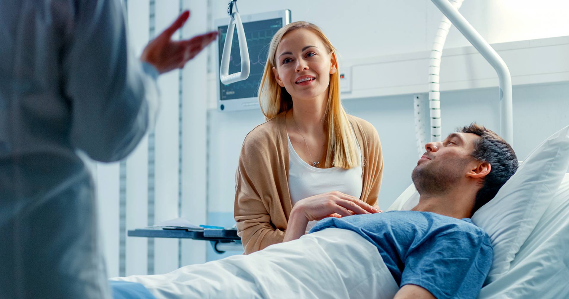 Kobieta z ulgą wysłuchuje lekarza, siedząc u boku hospitalizowanego mężczyzny